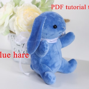 Könnte beinhalten: Ein blaues Plüschhasen-Spielzeug mit einem weißen Band um den Hals. Das Spielzeug sitzt auf einer weißen Oberfläche. Der Text "PDF tutorial toy" ist in schwarzen Buchstaben auf weißem Hintergrund über dem Spielzeug geschrieben. Der Text "Blue hare" ist in roten Buchstaben auf weißem Hintergrund unter dem Spielzeug geschrieben.