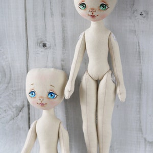 May include: Two handmade fabric dolls with painted faces and blue eyes. The dolls are unclothed and have sewn details. The doll on the left is sitting and the doll on the right is standing.