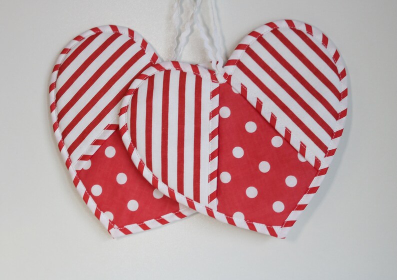 May include: Two red and white striped fabric hearts with white polka dots. The hearts are sewn together and have a white string attached to the top.