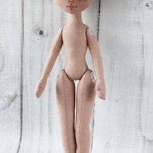 May include: A handmade doll with a beige fabric body, green eyes, and a painted face. The doll has button joints at the shoulders, elbows, hips, and knees.