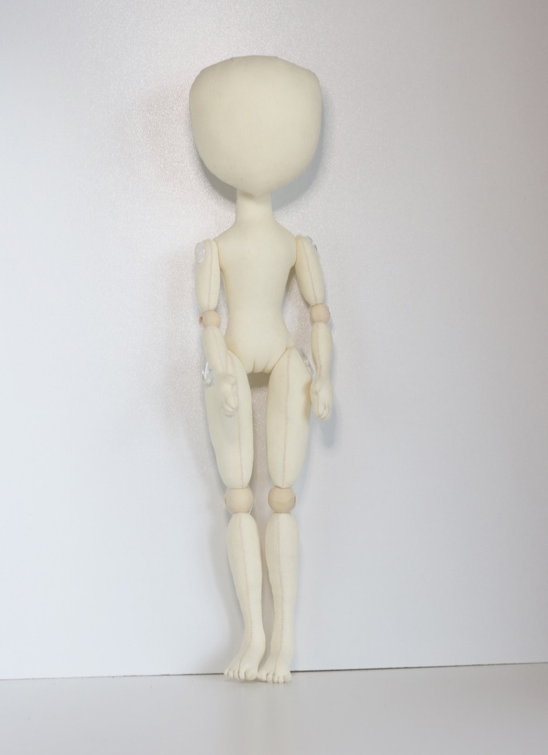 May include: A white fabric doll with wooden joints. The doll has a round head and no facial features. The doll is standing upright with its arms at its sides.