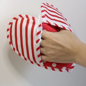 May include: Red and white striped oven mitt with a red and white polka dot lining. The mitt is being held by a hand.