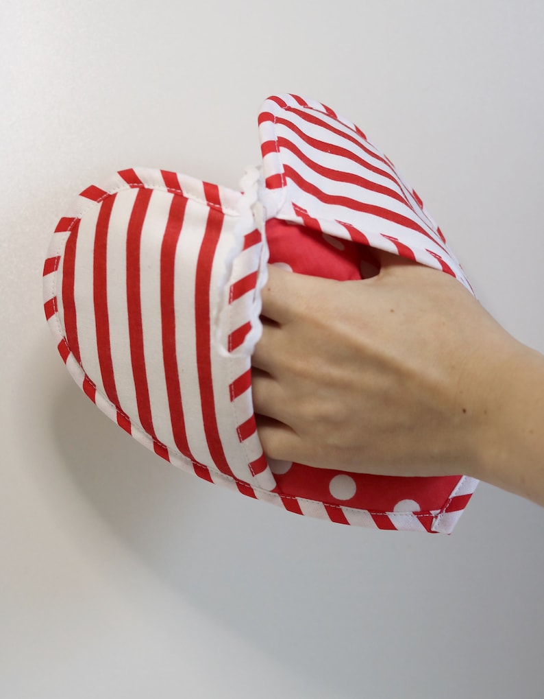 May include: Red and white striped oven mitt with a red and white polka dot lining. The mitt is being held by a hand.