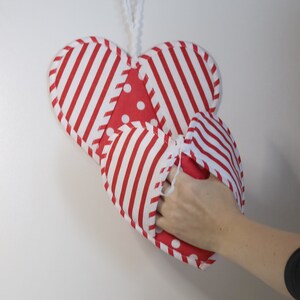 May include: Red and white striped heart-shaped oven mitt with white polka dots. The mitt is hanging from a white string.