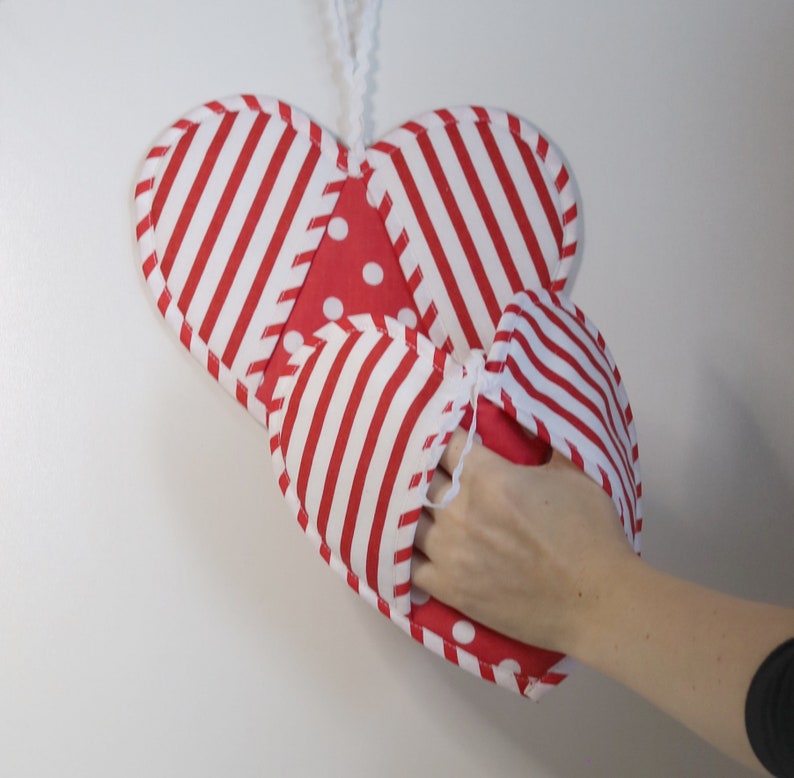 May include: Red and white striped heart-shaped oven mitt with white polka dots. The mitt is hanging from a white string.