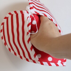 May include: Red and white striped oven mitt with a red and white polka dot lining. The mitt is folded in half and a hand is holding it open.