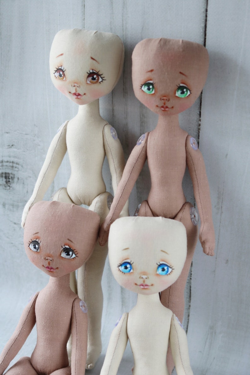May include: Four handmade cloth dolls with painted faces and button joints. The dolls are in various skin tones and have different colored eyes.