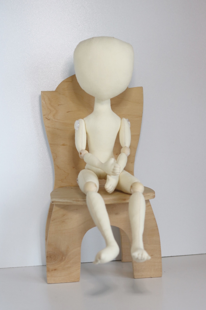May include: A white fabric doll with wooden joints sits on a wooden chair. The doll has a simple, round head and no facial features.