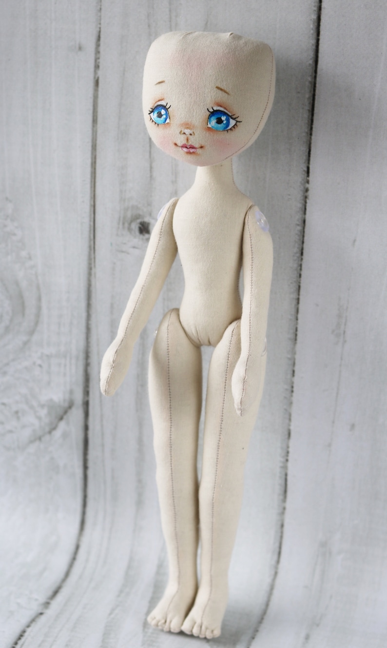 May include: A plain white fabric doll with blue eyes and a stitched face. The doll has a simple design with no clothing or accessories.