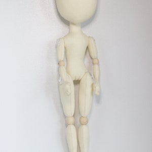 May include: A white fabric doll with wooden joints. The doll has a round head and no facial features. The doll is standing upright with its arms at its sides.