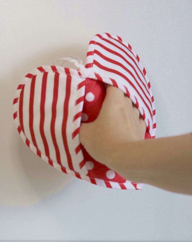 May include: A red and white striped heart-shaped fabric pouch with red polka dots on the inside. The pouch is being held open by a hand.