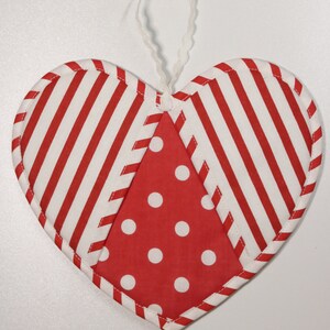 May include: Red and white striped heart-shaped fabric ornament with a red and white polka dot center. The ornament has a white loop for hanging.