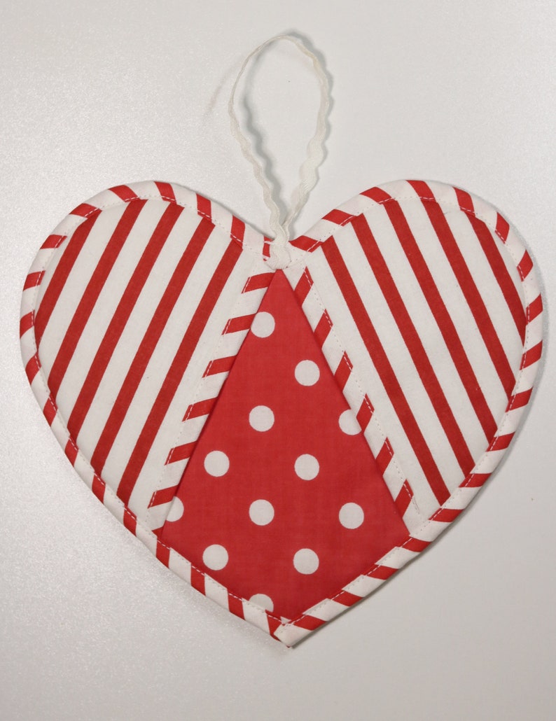 May include: Red and white striped heart-shaped fabric ornament with a red and white polka dot center. The ornament has a white loop for hanging.