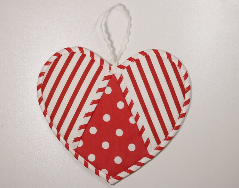 May include: A red and white striped heart-shaped ornament with a red and white polka dot center. The ornament has a white loop for hanging.