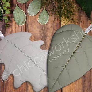 May include: Two leaf-shaped decorative pillows in light gray and olive green, with stitched vein details. The pillows are on a wooden surface with leaves and the text "CHICCA" in a circular logo.