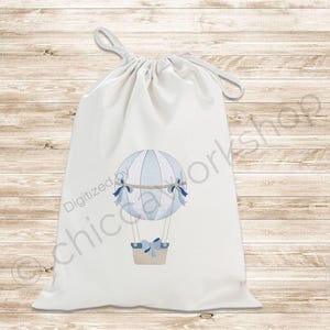 May include: A white drawstring bag featuring a watercolor illustration of a blue and white hot air balloon with a basket. The balloon has blue bows and a light brown basket. The bag has a light gray drawstring.
