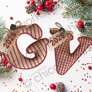 Può includere: Ornamenti natalizi decorativi a forma di lettere "G" e "V", con un motivo a righe e quadretti rossi e bianchi. Ogni ornamento ha un'etichetta con "2025". L'immagine include aghi di pino, bacche rosse e pigne.