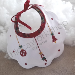 Può includere: Bavaglino bianco per neonati con bordo smerlato, decorato con pois rossi e ricami natalizi. Presenta un bordo a quadri rossi e verdi e ornamenti pendenti, tra cui una campana e un bastoncino di zucchero. Il bavaglino è legato con un nastro rosso.