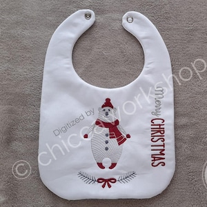 Op de afbeelding: Witte baby slabbetje met een kerstthema. Het heeft een geborduurde ijsbeer met een rode hoed en sjaal. De woorden "Merry Christmas" zijn verticaal in het rood geborduurd.