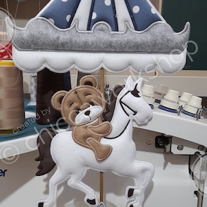 May include: A plush toy carousel horse with a brown teddy bear riding on top. The carousel horse is white with brown hooves and a brown mane. The carousel is decorated with a blue and white striped canopy.