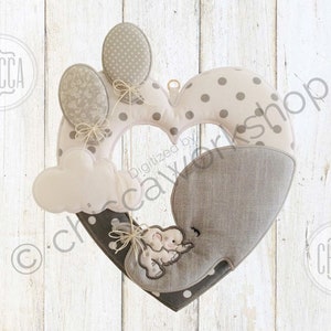 May include: A heart-shaped wreath with a grey and white polka dot pattern. The wreath features a grey elephant with a pink cloud and balloons. The wreath is decorated with a grey and white polka dot ribbon.