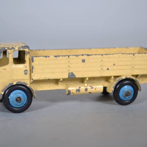 May include: A vintage yellow toy truck with a flatbed and blue wheels. The truck has a worn paint finish and is made of metal.