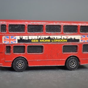 Può includere: Giocattolo di autobus a due piani rosso con la scritta "See More London" stampata sul lato. L'autobus ha una bandiera Union Jack su ogni lato e finestre nere.
