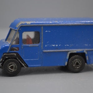 Puede incluir: Un camión de reparto de juguete azul con una franja blanca y ruedas negras. El camión tiene una cabina blanca y una caja de carga azul.