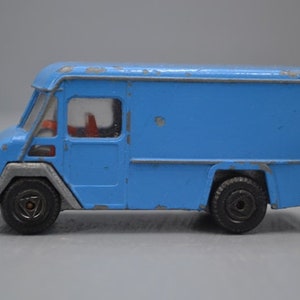 May include: A blue toy delivery truck with a white cab and a gray trim. The truck has a driver's side door and a rear door. The truck has black wheels.