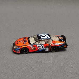 May include: A toy car model of a race car with the number 31 on the side. The car is orange, black, and blue with the word "Cingular" on the side.