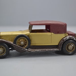 Può includere: Un modello di auto giocattolo dorata e marrone di una decappottabile d'epoca con capote marrone. L'auto ha una griglia anteriore e ruote dettagliate.