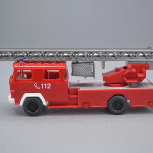 Op de afbeelding: Een rode speelgoedbrandweerwagen met een grijze ladder en een witte telefoon met het nummer 112 aan de zijkant.