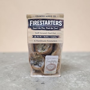 Könnte beinhalten: Eine transparente Plastiktüte mit sechs handgemachten Feueranzündern. Das Etikett trägt die Aufschrift "FIRESTARTERS" mit dem Text "Spark the Fire. Feed the Soul." und "6 Handmade Firestarters."