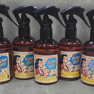 May include: Several brown spray bottles with black spray nozzles are arranged in a row. Each bottle has a label with the words "FUNK OFF" and a vintage-style illustration of a woman. The labels also include the names of different scents.