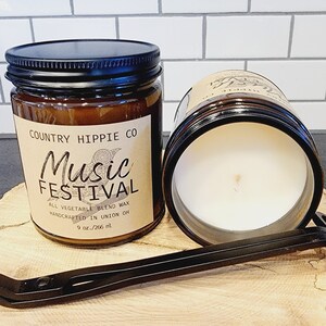 Könnte beinhalten: Ein braunes Glasgefäß für eine Kerze mit einem schwarzen Deckel. Das Etikett ist braun mit weißem Text, der "COUNTRY HIPPIE CO Music FESTIVAL ALL VEGETABLE BLEND WAX HANDCRAFTED IN UNION OH 9 oz./266 ml" lautet.