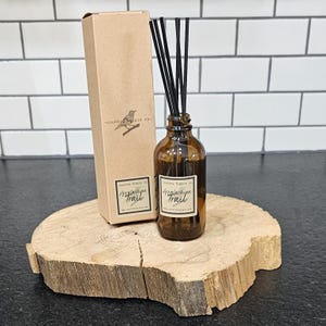 May include: A brown glass bottle with black reeds and a label that reads "Country Hippie Co. Appalachian Trail" is sitting on a wooden slice. The bottle is packaged in a brown cardboard box with the same label.