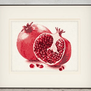 Puede incluir: Dos granadas rojas, una entera y otra cortada por la mitad, mostrando las semillas rojas en su interior. Las granadas están sobre un fondo blanco.