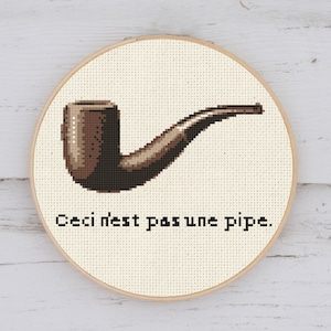Peut inclure: Un tuyau brodé en brun et noir sur un fond blanc avec le texte "Ceci n'est pas une pipe."