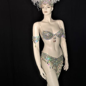 May include: A white feather headdress with a silver and iridescent crystal bra and matching skirt. The costume is worn by a mannequin.