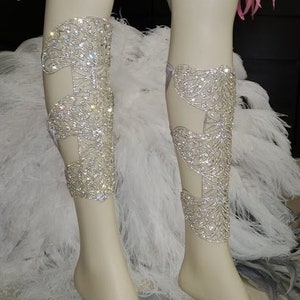 Puede incluir: Un par de brazaletes de pierna plateados con un dise&ntilde;o delicado e intrincado. Los brazaletes est&aacute;n adornados con brillantes pedrer&iacute;a y se llevan en las piernas de un maniqu&iacute;.