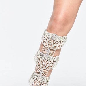 Puede incluir: Un brazalete de pierna plateado con un dise&ntilde;o delicado e intrincado que presenta m&uacute;ltiples capas de adornos de cristal. El brazalete se lleva en la pierna de una persona, extendi&eacute;ndose desde el tobillo hasta la rodilla.