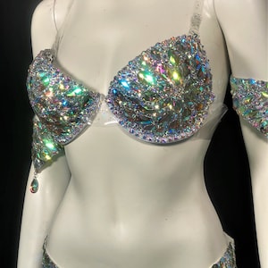 May include: A two-piece iridescent crystal costume set with a bra and a skirt. The bra has clear straps and the skirt has a high waist.
