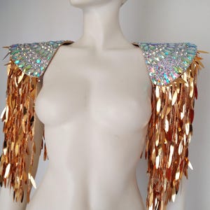 May include: A pair of shoulder epaulets featuring iridescent, multi-faceted crystals on the top panels. Long, dangling gold-toned metallic leaf-shaped sequins hang from the edges, creating a fringe effect that covers the upper arms.