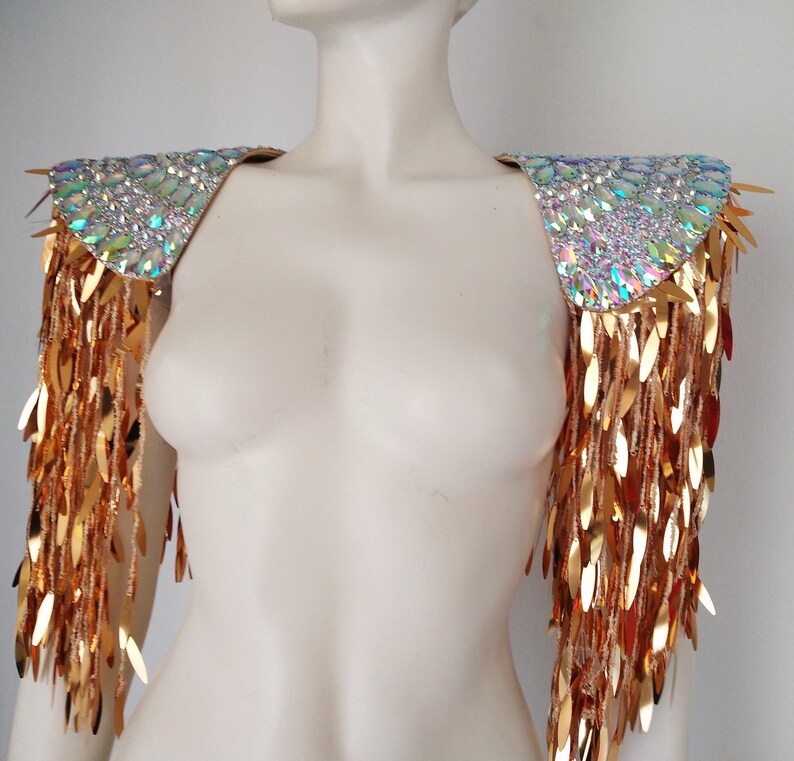 May include: A pair of shoulder epaulets featuring iridescent, multi-faceted crystals on the top panels. Long, dangling gold-toned metallic leaf-shaped sequins hang from the edges, creating a fringe effect that covers the upper arms.