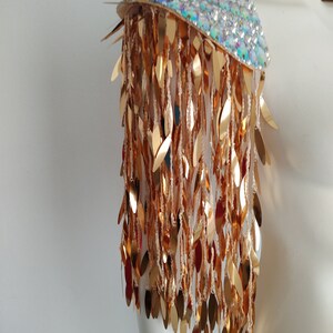May include: A gold sequined shoulder piece with a iridescent base. The sequins are shaped like leaves and hang down in a fringe.