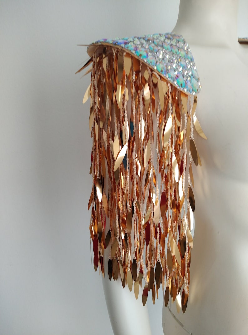May include: A gold sequined shoulder piece with a iridescent base. The sequins are shaped like leaves and hang down in a fringe.