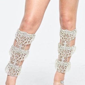 Puede incluir: Un par de pu&ntilde;os de pierna blancos con un dise&ntilde;o delicado e intrincado hecho de diamantes de imitaci&oacute;n. Los pu&ntilde;os est&aacute;n superpuestos y presentan un borde festoneado.