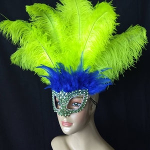 Pode incluir: Uma m&aacute;scara de carnaval verde e azul com pedrarias e um grande adere&ccedil;o de penas verdes.