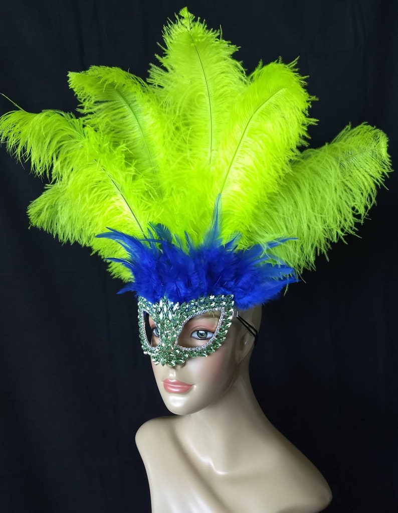Pode incluir: Uma m&aacute;scara de carnaval verde e azul com pedrarias e um grande adere&ccedil;o de penas verdes.