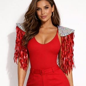 May include: A bright red sleeveless bodysuit paired with matching high-waisted trousers featuring a belt. The garment includes detachable shoulder epaulets adorned with iridescent crystals and long, dangling red sequin fringe accents.